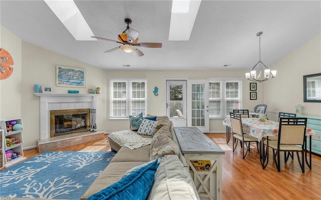 living room featuring lofted ceiling with skylight, ceiling fan with notable chandelier, light wood finished floors, and a tile fireplace