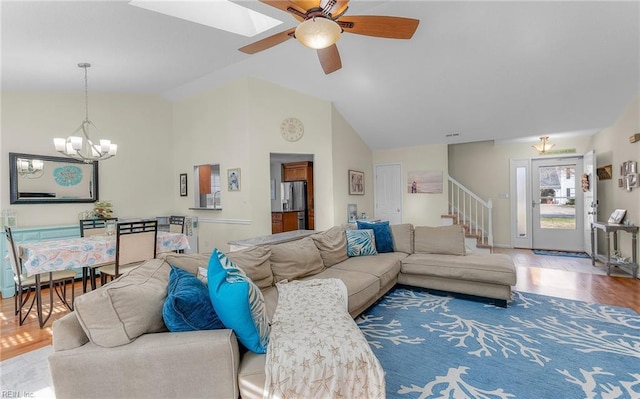 living room with ceiling fan with notable chandelier, stairway, vaulted ceiling with skylight, and wood finished floors