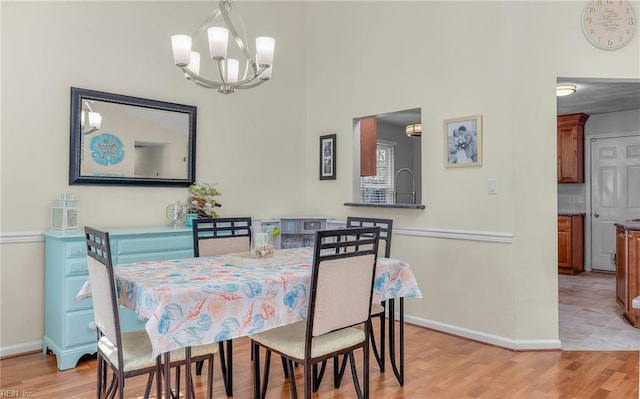 dining room featuring a notable chandelier, light wood-style flooring, baseboards, and a towering ceiling