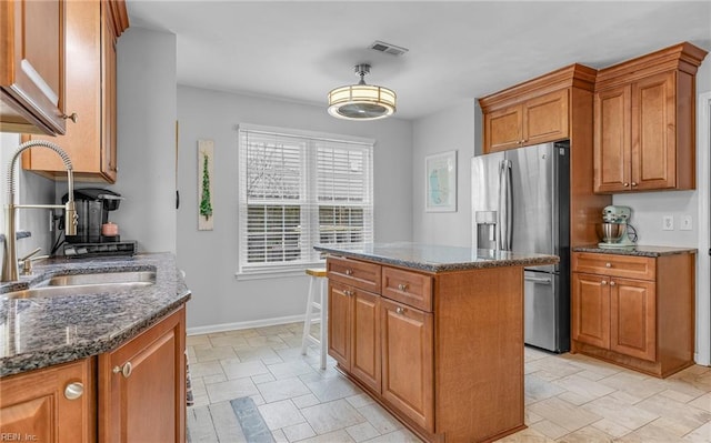 kitchen with visible vents, a center island, brown cabinets, stainless steel fridge, and a sink