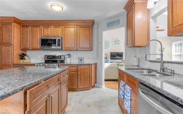 kitchen with brown cabinetry, light stone countertops, stainless steel appliances, and a sink