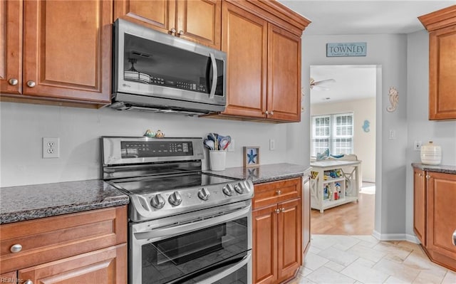 kitchen featuring dark stone countertops, stainless steel appliances, brown cabinets, and a ceiling fan