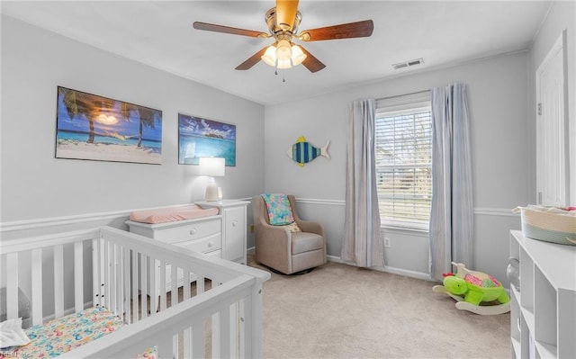 bedroom with visible vents, a crib, baseboards, light colored carpet, and a ceiling fan