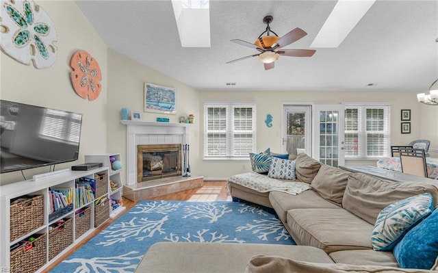 living area with lofted ceiling, ceiling fan with notable chandelier, a tile fireplace, wood finished floors, and a textured ceiling