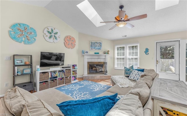 living room featuring vaulted ceiling with skylight, a tile fireplace, a textured ceiling, and ceiling fan