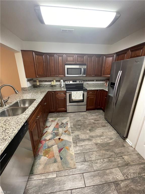 kitchen with a sink, visible vents, light stone countertops, and appliances with stainless steel finishes