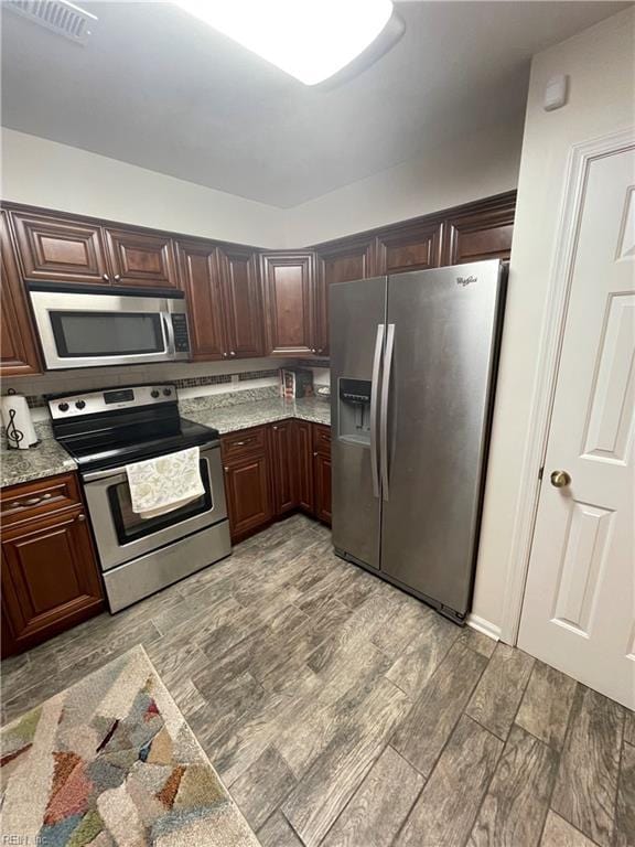 kitchen with light wood-style flooring, light stone counters, visible vents, and appliances with stainless steel finishes