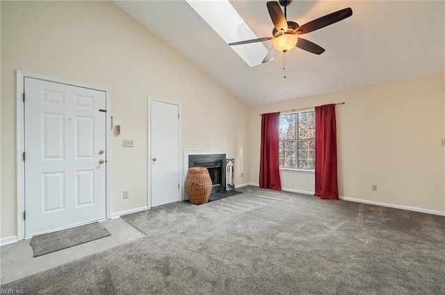 unfurnished living room featuring a fireplace with flush hearth, carpet flooring, a skylight, high vaulted ceiling, and a ceiling fan