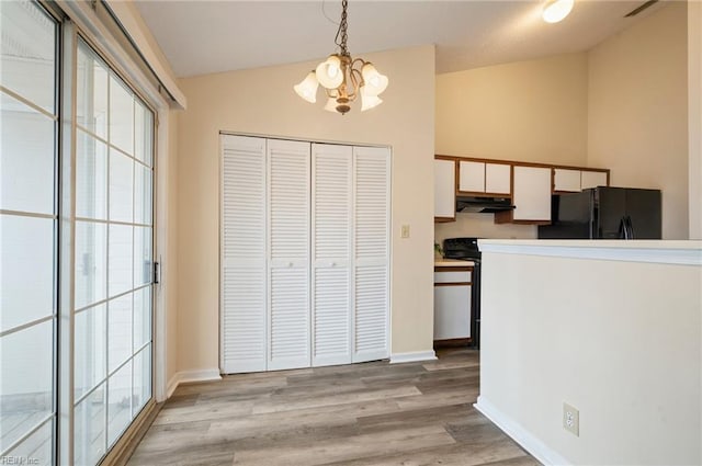 kitchen with under cabinet range hood, lofted ceiling, light wood-style flooring, freestanding refrigerator, and hanging light fixtures