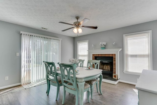 dining space featuring visible vents, a brick fireplace, baseboards, and wood finished floors