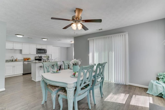 dining space with light wood-type flooring, baseboards, a textured ceiling, and visible vents