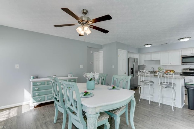 dining space featuring ceiling fan, baseboards, a textured ceiling, and light wood-style flooring