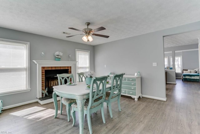 dining room featuring visible vents, baseboards, a fireplace, wood finished floors, and a textured ceiling