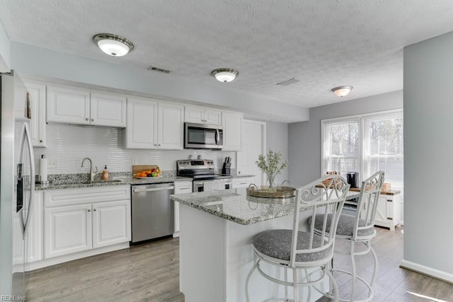 kitchen with light wood finished floors, visible vents, appliances with stainless steel finishes, white cabinetry, and a sink