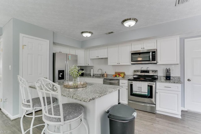 kitchen with visible vents, light wood-style flooring, a sink, white cabinets, and appliances with stainless steel finishes