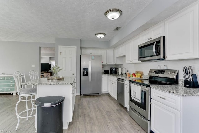 kitchen with visible vents, a sink, a kitchen island, appliances with stainless steel finishes, and light wood finished floors