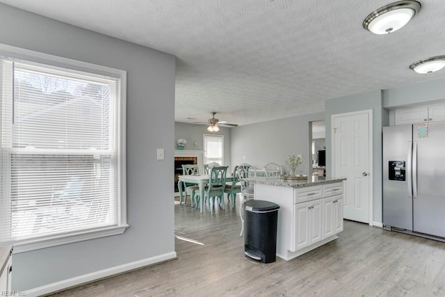 kitchen with white cabinetry, stainless steel fridge, light wood-style floors, a fireplace, and baseboards