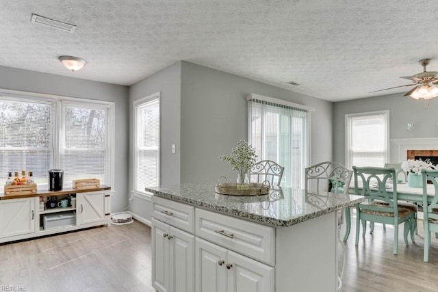 kitchen with visible vents, light wood-style flooring, light stone counters, a kitchen island, and white cabinetry