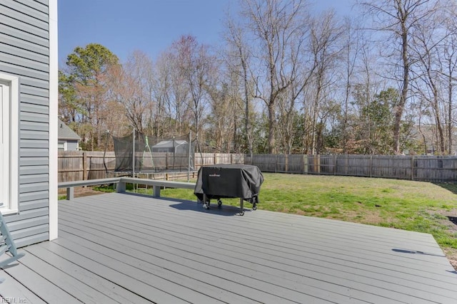 deck with a yard, a trampoline, a fenced backyard, and grilling area