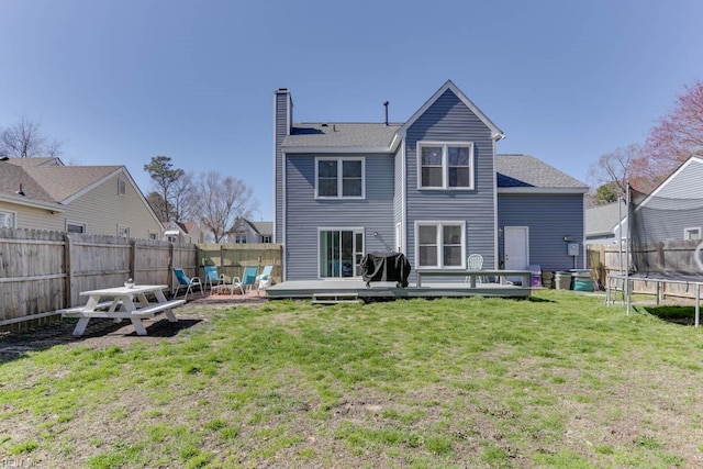 rear view of property featuring a trampoline, a lawn, a chimney, a fenced backyard, and a deck