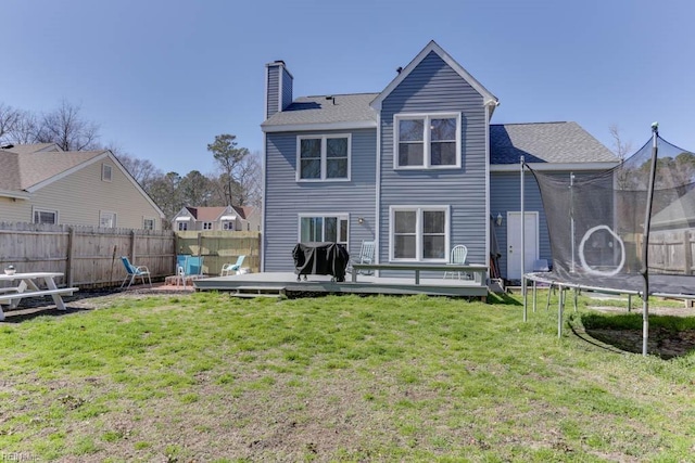 back of property featuring a lawn, a trampoline, a wooden deck, fence private yard, and a chimney