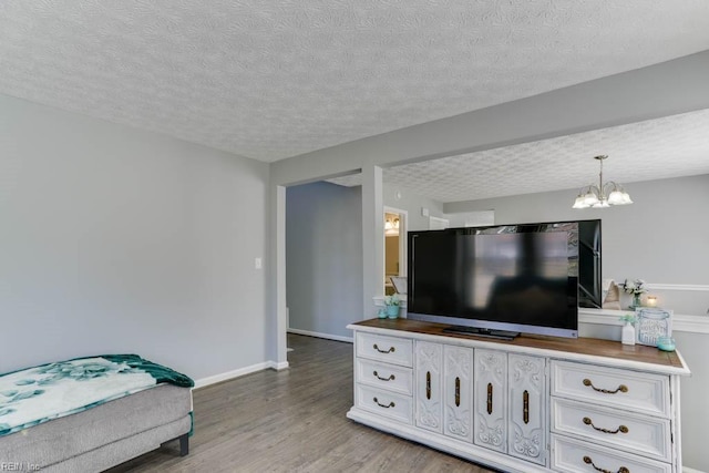 living room with an inviting chandelier, wood finished floors, baseboards, and a textured ceiling