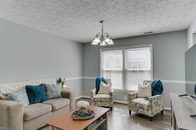 living room with visible vents, baseboards, a chandelier, wood finished floors, and a textured ceiling