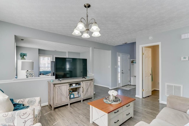 living room featuring light wood-type flooring, visible vents, baseboards, and a notable chandelier