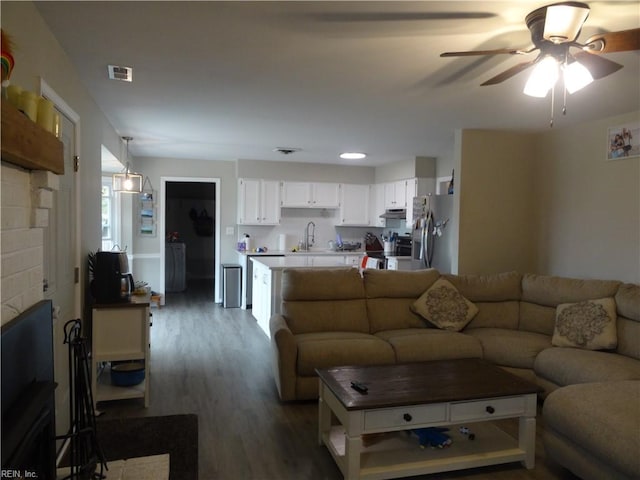 living area with ceiling fan, visible vents, wood finished floors, and a fireplace