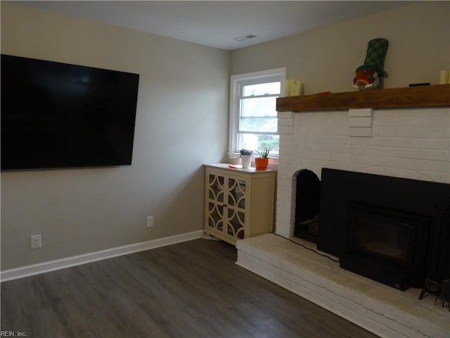 living room featuring visible vents, baseboards, a brick fireplace, and wood finished floors