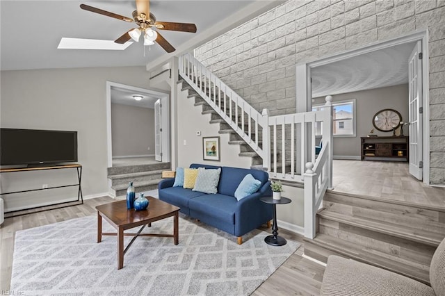 living room featuring stairs, wood finished floors, a ceiling fan, and lofted ceiling with skylight