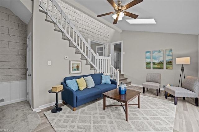 living room with stairway, vaulted ceiling with skylight, a ceiling fan, and wood finished floors