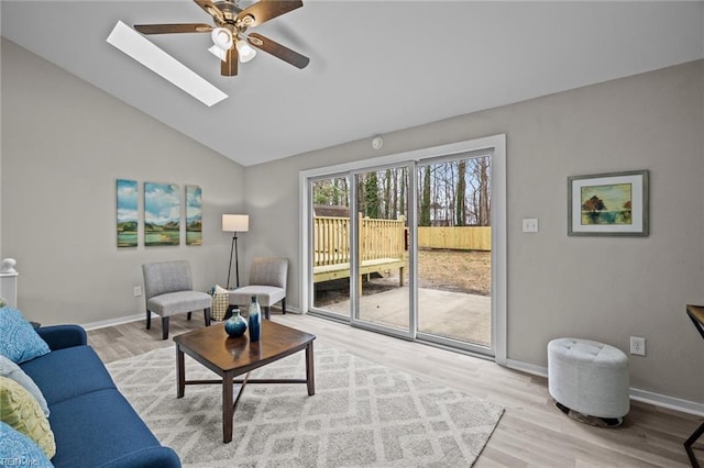 living area with vaulted ceiling with skylight, baseboards, ceiling fan, and wood finished floors