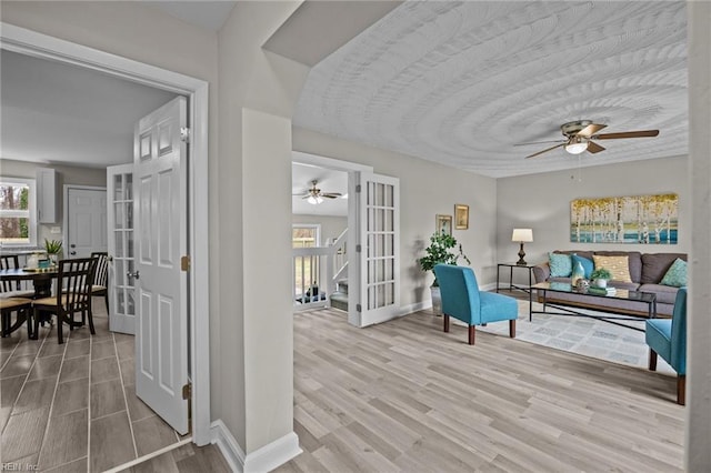 living area with stairway, wood finished floors, baseboards, and ceiling fan