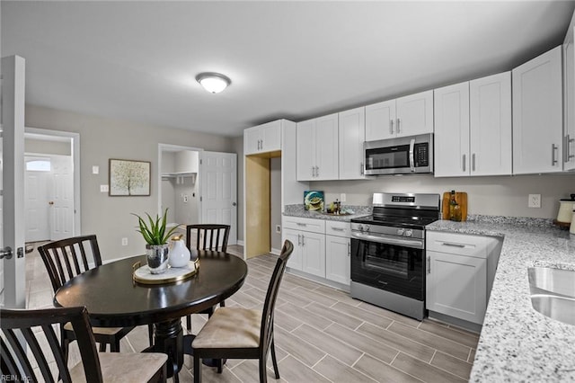 kitchen with light stone counters, wood tiled floor, a sink, appliances with stainless steel finishes, and white cabinetry