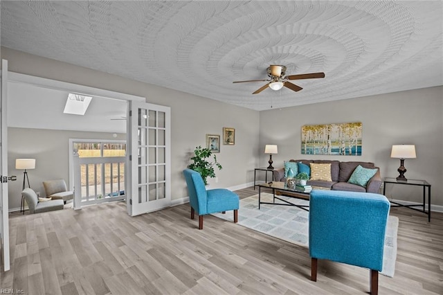 living room featuring baseboards, a skylight, ceiling fan, and wood finished floors