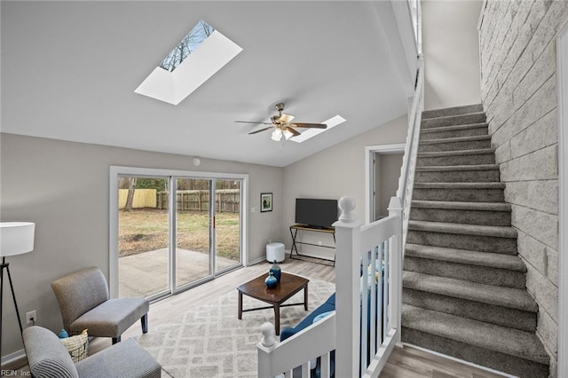 living room with lofted ceiling with skylight, a ceiling fan, wood finished floors, stairway, and baseboards