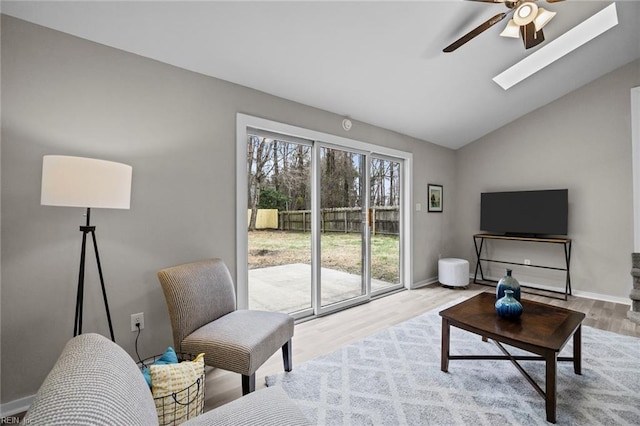 living area featuring vaulted ceiling with skylight, baseboards, a ceiling fan, and wood finished floors