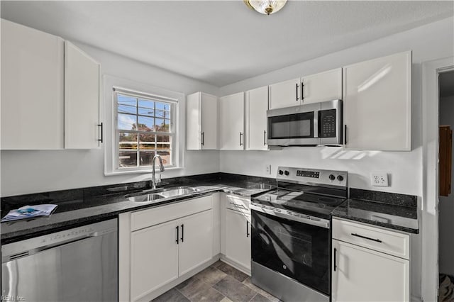 kitchen featuring a sink, stainless steel appliances, dark stone countertops, and white cabinetry