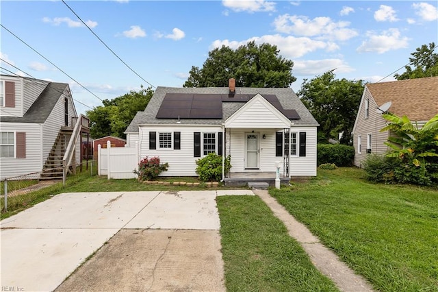 view of front facade featuring roof mounted solar panels, roof with shingles, a front lawn, and fence