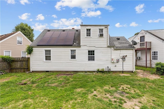 back of property with roof mounted solar panels, a lawn, roof with shingles, and fence