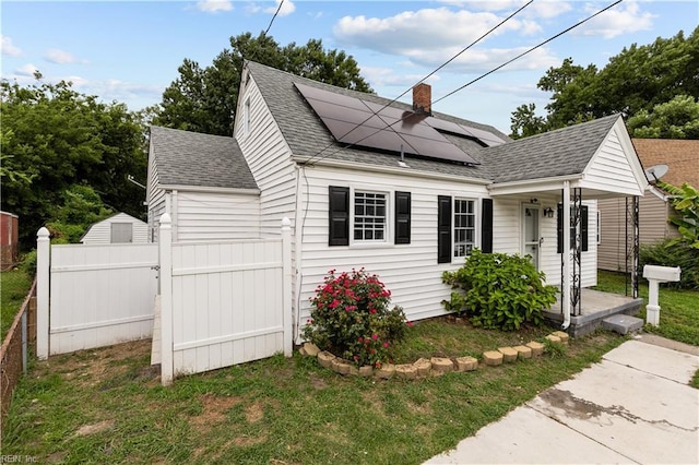 view of front of property with fence, roof with shingles, covered porch, solar panels, and a chimney