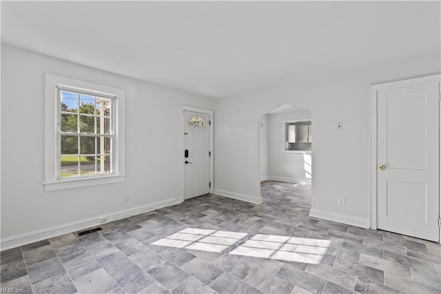 foyer featuring baseboards, arched walkways, visible vents, and stone finish floor