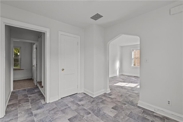 unfurnished room featuring baseboards, arched walkways, visible vents, and stone finish floor