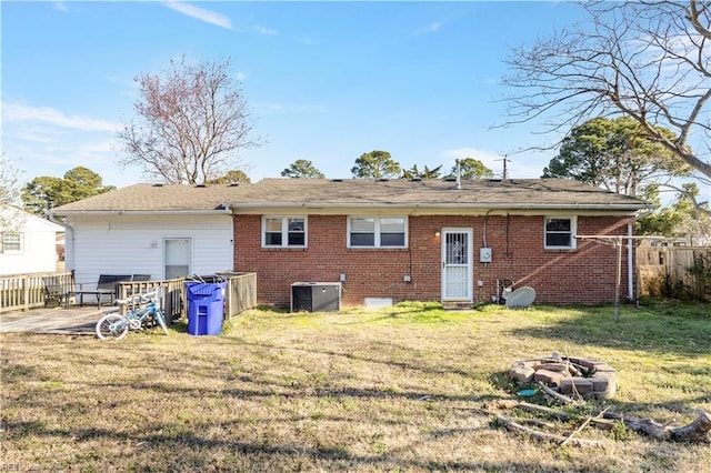 rear view of house with central AC, an outdoor fire pit, fence, a yard, and brick siding