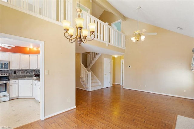 kitchen with ceiling fan with notable chandelier, white cabinetry, stainless steel appliances, light wood finished floors, and decorative backsplash