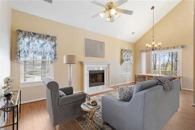 living area featuring ceiling fan with notable chandelier, wood finished floors, baseboards, and a high end fireplace