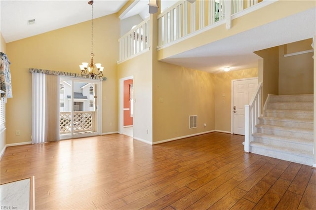 unfurnished living room with stairs, an inviting chandelier, wood finished floors, and baseboards