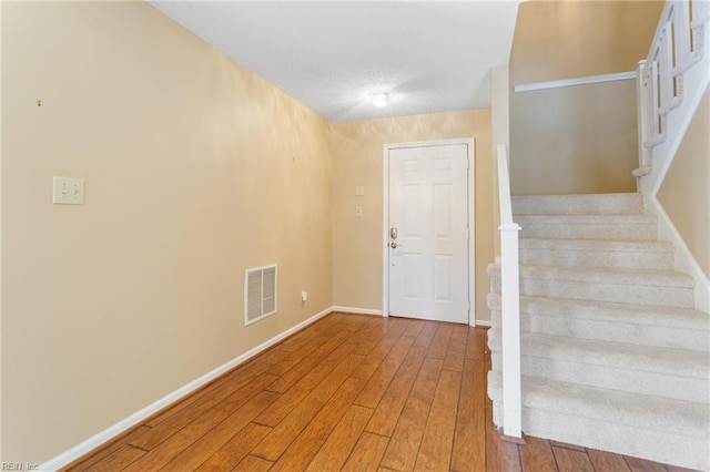 foyer with stairway, baseboards, visible vents, and wood-type flooring