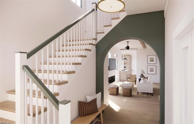 stairs featuring a high ceiling, wood finished floors, arched walkways, and ceiling fan